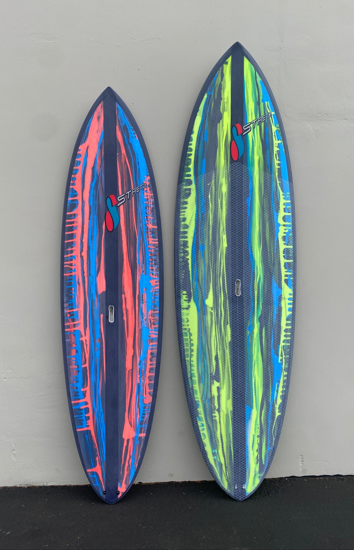 Two colorful surfboards with abstract patterns on a gray surface.
